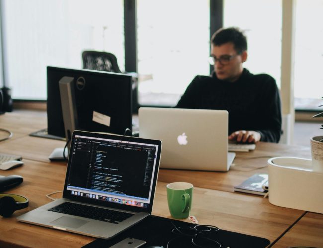 A web developer working on code in a modern office setting with multiple devices.
